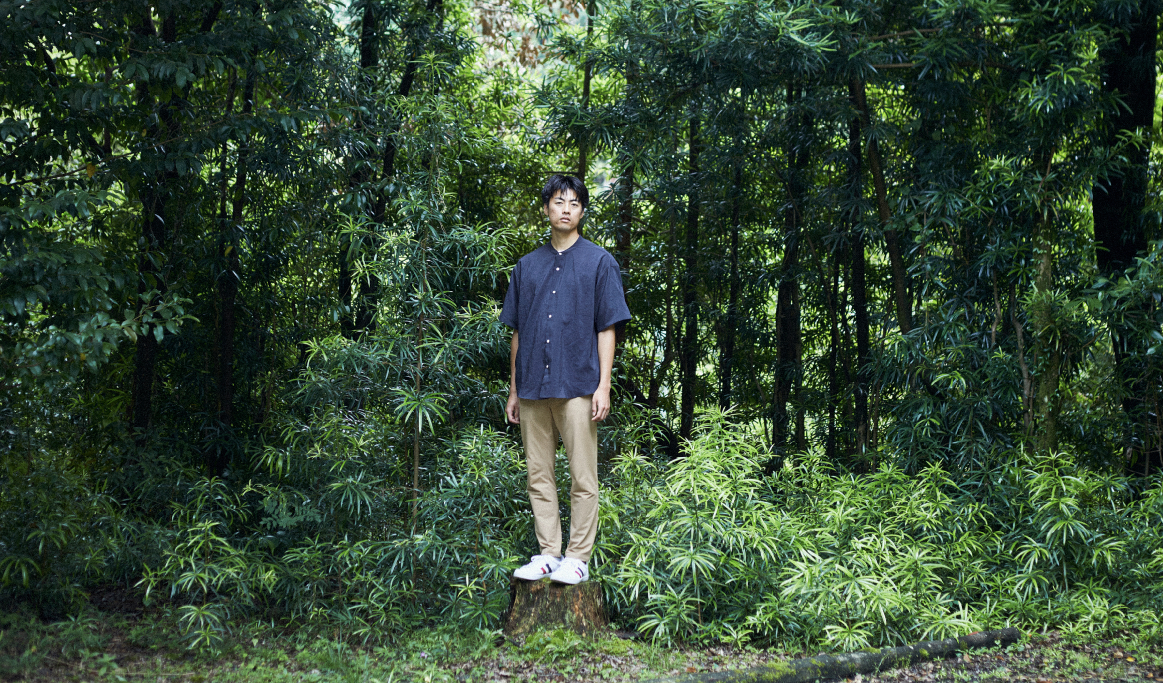 草木の前で青年がこちらを見ている
