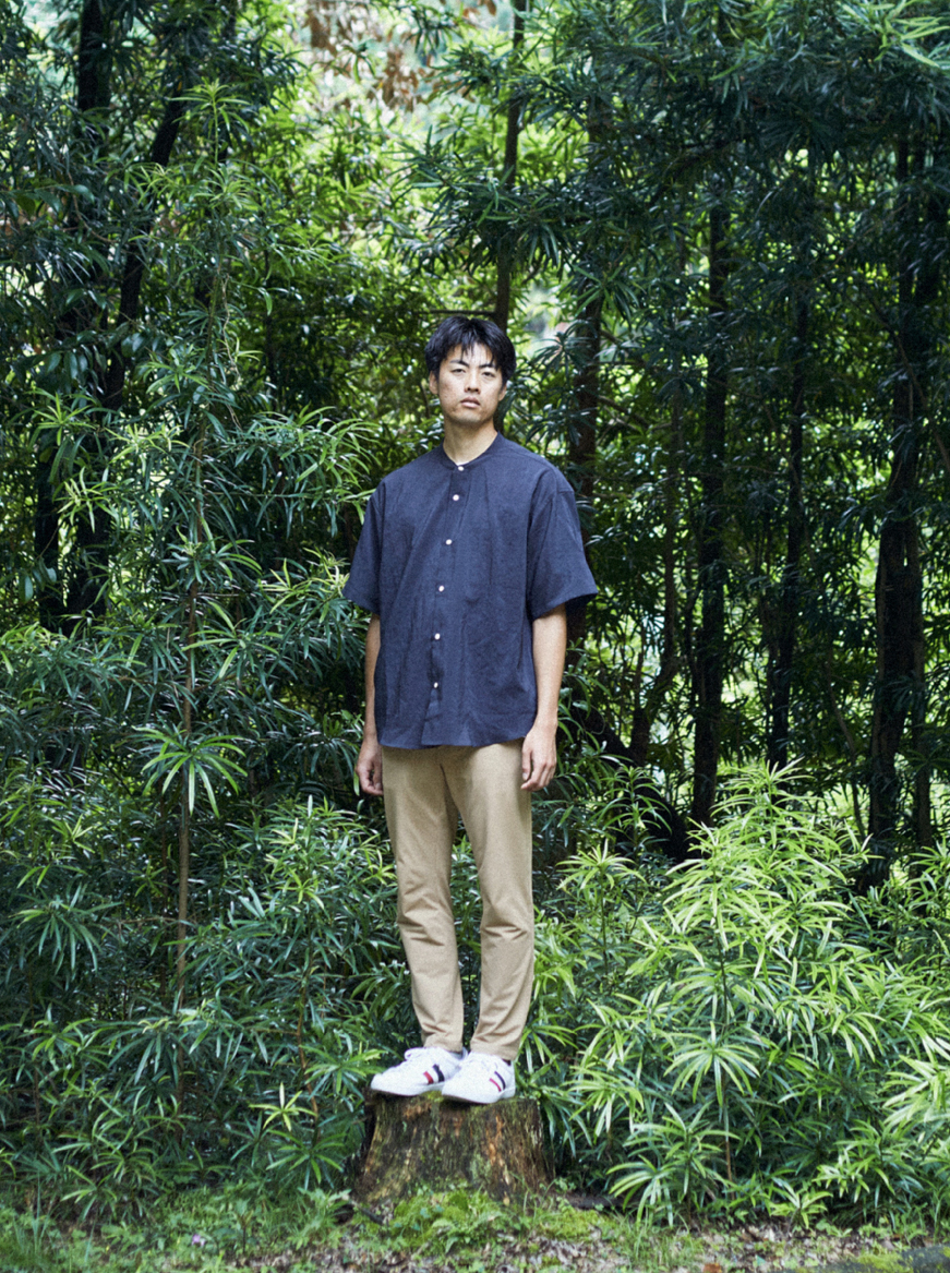 草木の前で青年がこちらを見ている